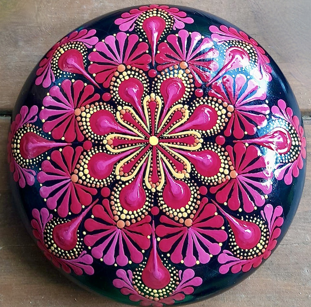 Round stone painted with pink and gold mandala dot patterns in radiating floral design