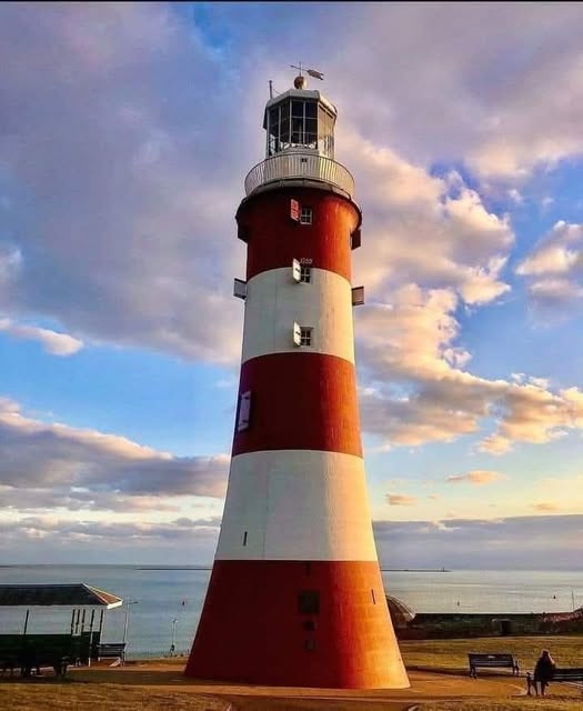 Tall red and white striped lighthouse near the sea under a blue and golden cloudy sky