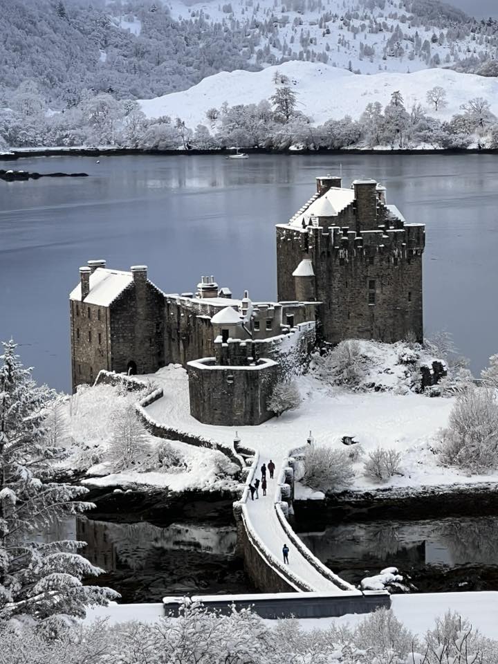 Snow-covered Scottish castle on a loch island with a causeway in winter landscape
