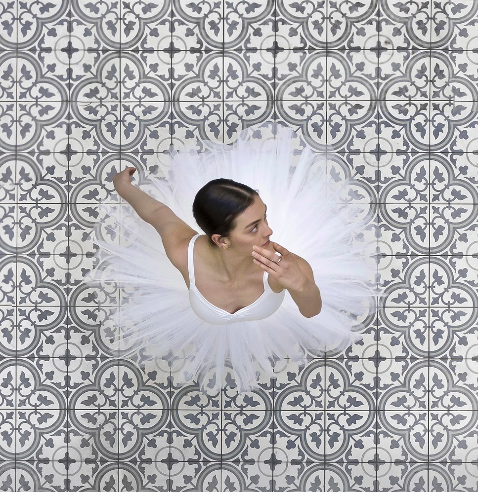 Overhead view of a ballerina in a white tutu on a patterned tile floor