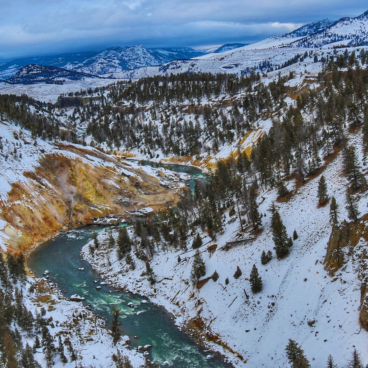 Turquoise river winding through a snowy mountain valley with evergreen trees