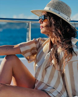 Woman in striped shirt and straw hat sitting on a yacht deck with ocean in background