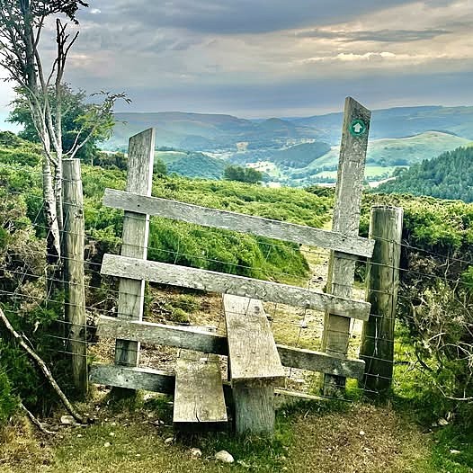 Rustic wooden stile on a footpath with green hills and a cloudy valley in the background