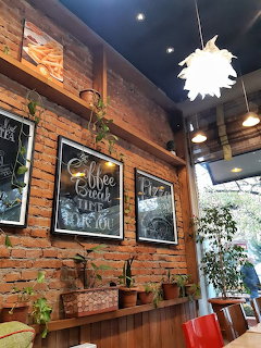 Warm cafe interior with exposed brick walls, hanging plants, chalkboard signs, and white pendant lamp