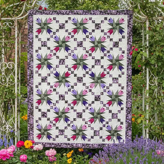 Patchwork quilt with floral star blocks hanging in a garden with colorful flowers