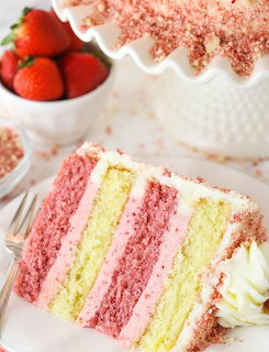 Slice of pink and white layered strawberry cake with crumb topping and fresh strawberries