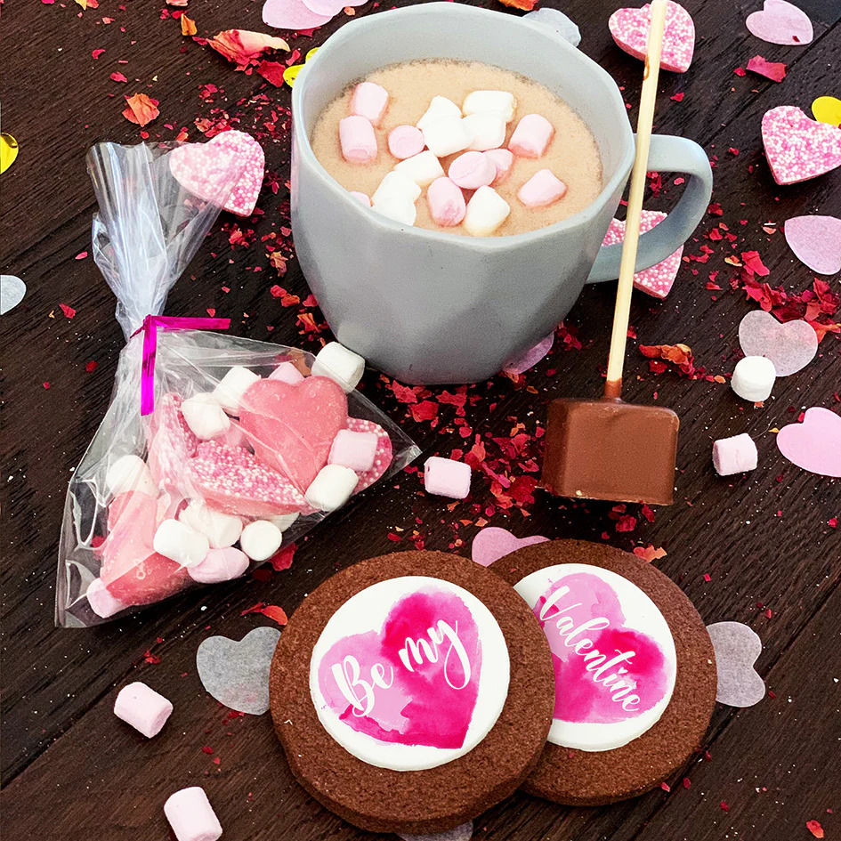 Hot chocolate with marshmallows, heart cookies, and Valentine candies on a wooden table