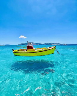 Yellow boat floating on clear turquoise sea with distant islands under a blue sky