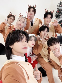 K-pop group in reindeer antlers and Santa outfits posing for a Christmas group selfie