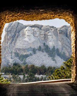 Mount Rushmore viewed through a rocky cave opening with trees in the foreground