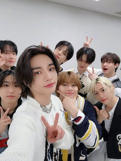Eight young men from K-pop group Stray Kids posing together for a group photo, making peace signs