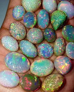 Hand holding multiple polished Ethiopian opal gemstones with rainbow iridescent colors