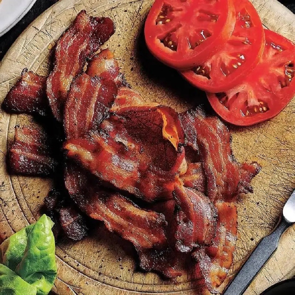 Cooked bacon, sliced tomatoes, and lettuce on a wooden cutting board