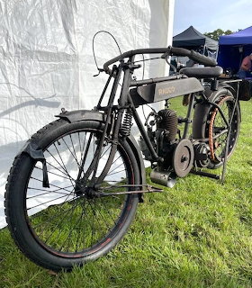 Vintage black Radco motorcycle parked on green grass under a white tent at an outdoor show