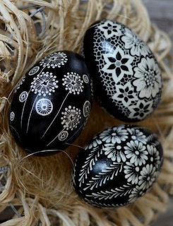Three black Easter eggs with white floral patterns in straw nest