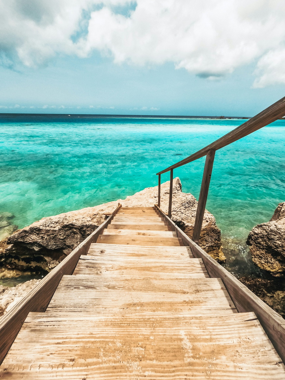 Wooden pier with railing leading into turquoise tropical ocean water under blue sky