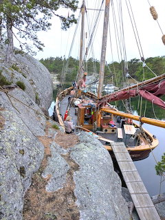 Wooden sailing trawler moored next to steep rocky cliff with masts and rigging visible