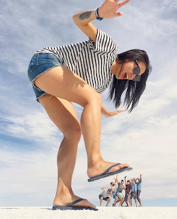 Woman in striped shirt and denim shorts posing in forced perspective over small people on salt flat