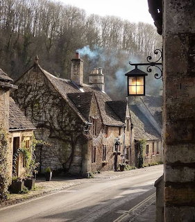 Old stone village houses along a quiet road with a glowing lantern and leafless trees