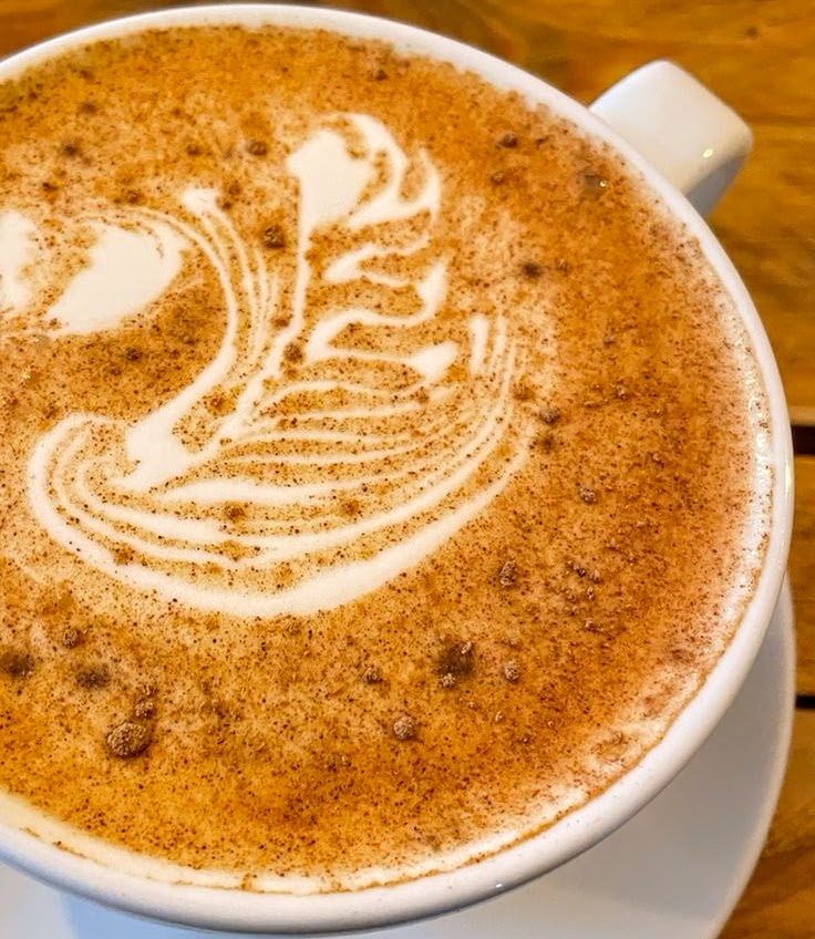 Latte art swan design in milk foam with brown powder dusting on coffee in white cup