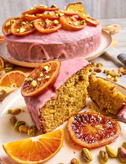 Blood orange and pistachio cake with pink frosting, citrus slices, and a cut slice on a plate