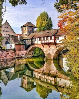 Historic half-timbered bridge house over a river with autumn trees and mirrored reflection