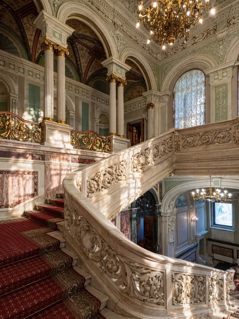 Ornate interior staircase with marble railings, chandeliers, and arched ceilings