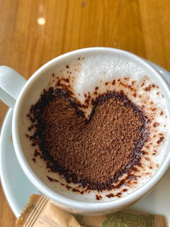 White cup of cappuccino with cocoa powder heart on milk foam on a saucer