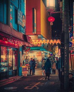 Narrow Tokyo street at dusk with illuminated shops, red lanterns, and pedestrians walking along colorful buildings