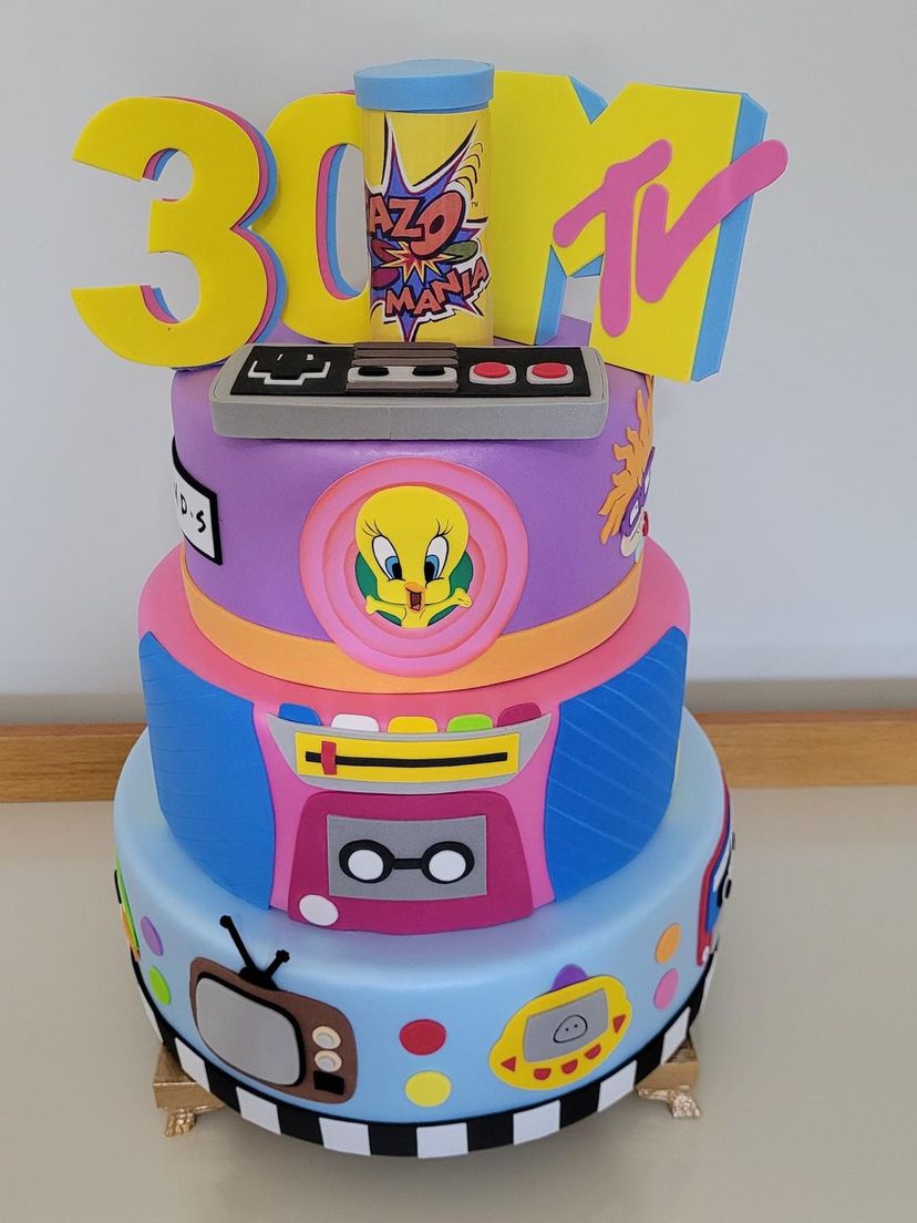 Three-tier birthday cake with 90s theme featuring MTV logo, Tweety Bird, retro TV and boombox decorations