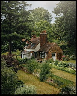 Aerial view of a quaint brick cottage with gardens and lawn surrounded by trees