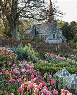 Stone church building with garden of pink and yellow tulips in foreground, surrounded by trees