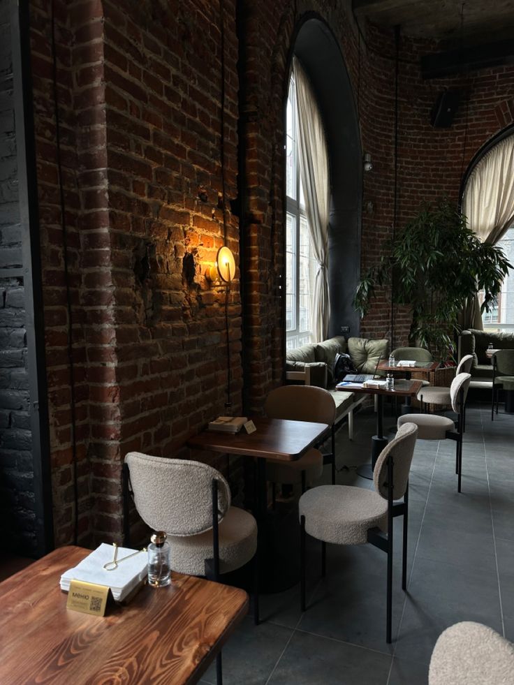 Cafe interior with brick walls, wooden tables, white chairs, and tall windows letting in natural light