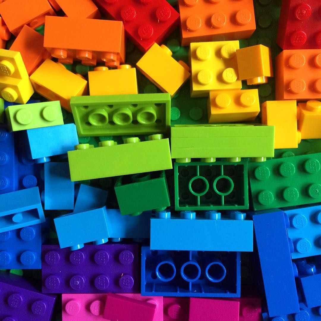 Pile of colorful plastic building blocks arranged in rainbow spectrum from warm to cool colors