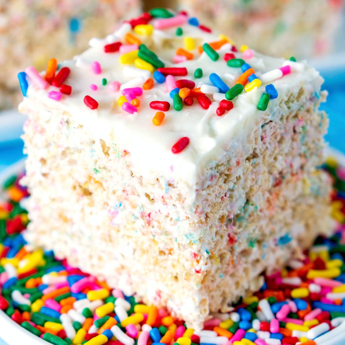 Slice of white funfetti cake with frosting and rainbow sprinkles on a sprinkle-covered plate