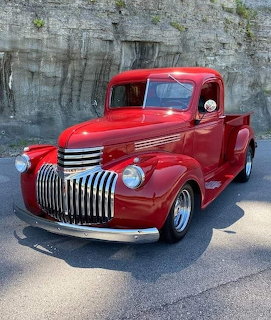 Restored red classic Chevrolet pickup truck with chrome grille parked outdoors near a rock wall