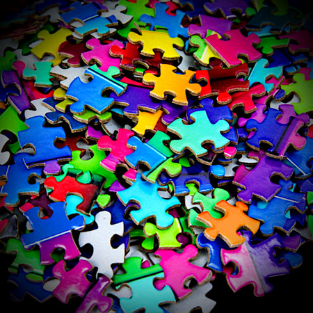 Pile of scattered colorful jigsaw puzzle pieces in many bright colors