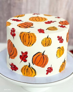 Round white cake decorated with orange pumpkins and red fall leaves