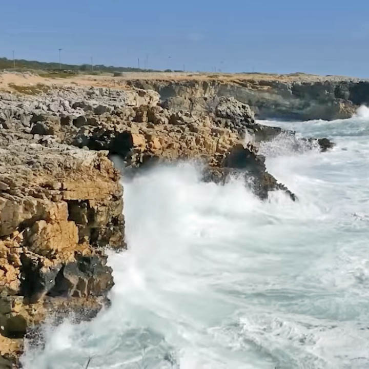 Rocky coastal cliffs with powerful waves crashing against brown stone formations creating white sea spray