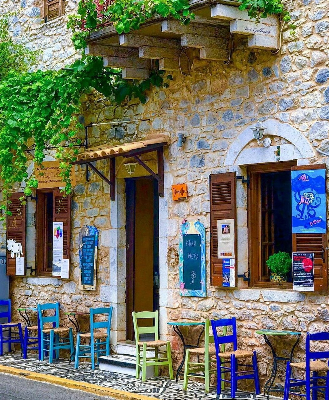 Greek tavern exterior with blue chairs on cobblestone street and stone building