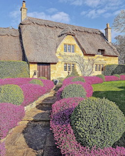 Yellow thatched roof cottage with colorful flowering garden and stone path under blue sky