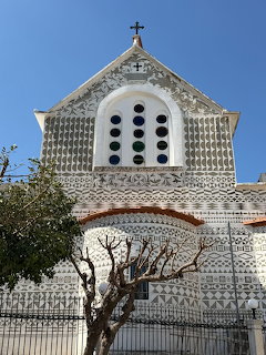 White ornate church facade with circular windows and decorative stonework against blue sky