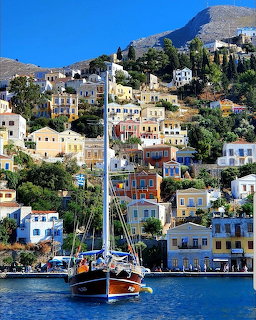 Colorful neoclassical houses on a hillside in Symi, Greece with a sailboat in the harbor