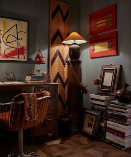 Eclectic interior corner with leather chair, floor lamp, stacked books, chevron screen, and abstract wall art
