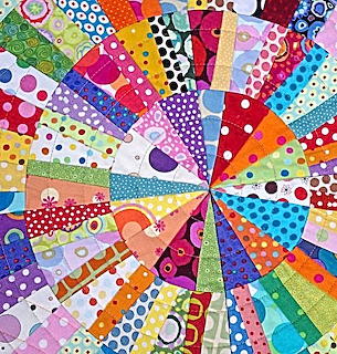 Colorful patchwork quilt with triangular fabric pieces radiating from center in rainbow colors with various patterns