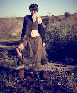 Woman in black jacket and long tulle skirt posing in arid desert landscape with dry brush