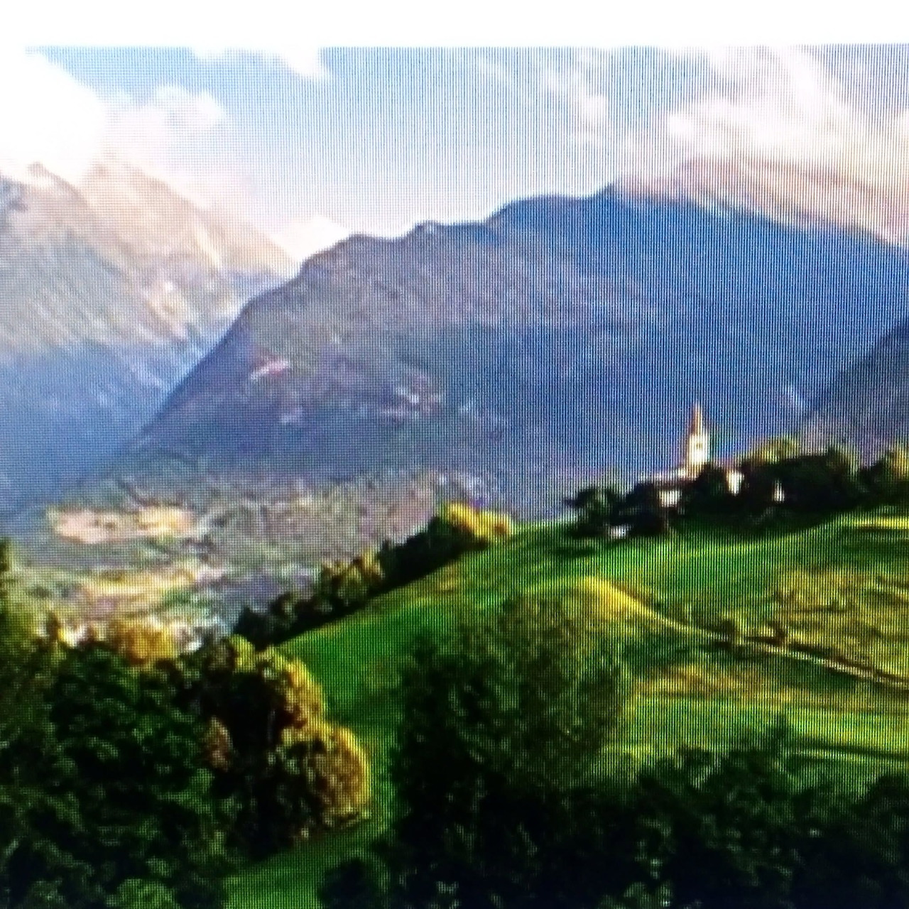 Green hillside with a church and mountain range under a bright sky