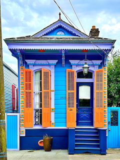 Colorful small house with blue walls, orange striped shutters, purple decorative trim, and front steps