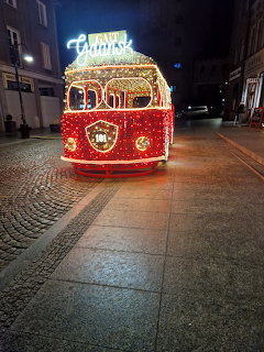 Brightly lit red vintage tram with Christmas decorations on a cobblestone street at night