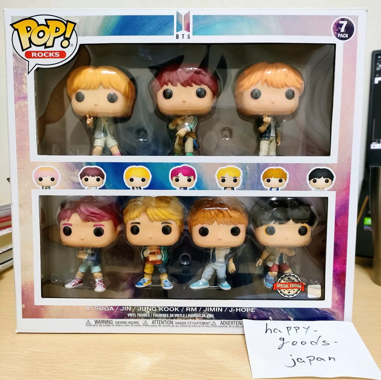 Seven BTS Funko Pop figures in a display box showing all seven members with colorful hair and casual outfits